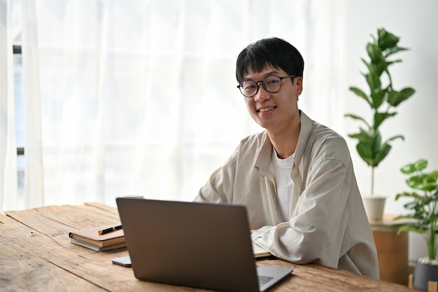 Retrato de jovem asiático trabalhando com laptop na sala de estar