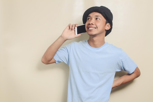 Retrato de jovem asiático vestindo camiseta azul e chapéu preto falando no telefone