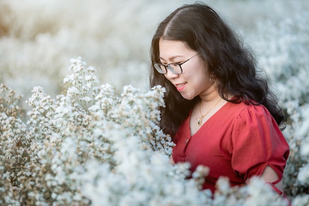 Retrato de jovem asiático viajante feliz com vestido vermelho desfrutando de flores brancas ou campo de flores brancas margarita no jardim natural de em Chiang Mai, Tailândia, viagens relaxam conceito de férias