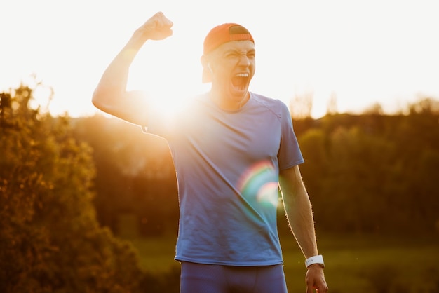 Retrato de jovem atleta masculino em forma desfrutando da vitória na maratona ao ar livre corredor bonito vencer a competição levantar a mão e gritar desfrutar de sucesso conceito de esporte e pessoas