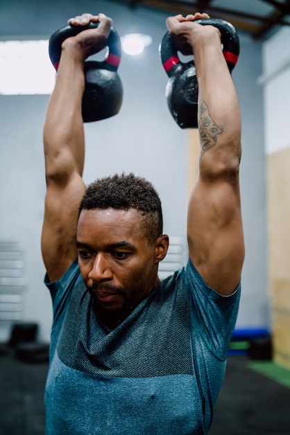 Retrato de jovem Atlético fazendo exercícios com crossfit kettlebel no ginásio. Crossfit, esporte e conceito de estilo de vida saudável.