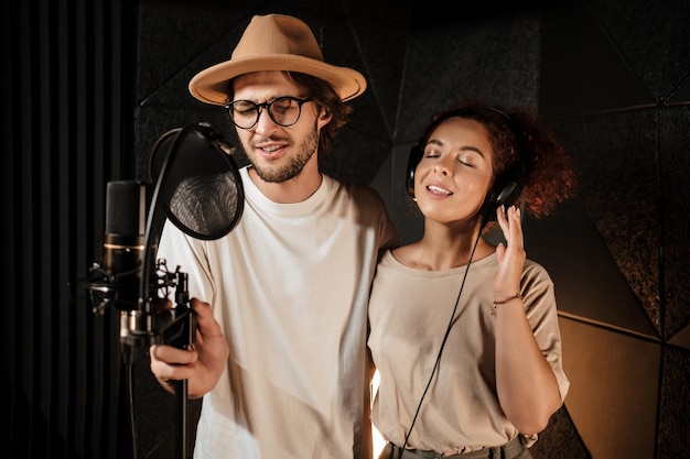 Retrato de jovem atraente e mulher cantando sensualmente juntos gravando música no estúdio moderno