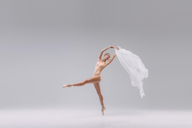 Retrato de jovem bailarina dançando com tecido transparente branco isolado sobre estúdio cinza