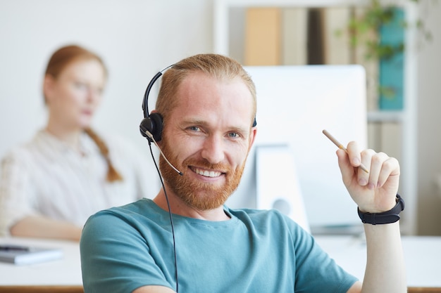 Retrato de jovem barbudo com fone de ouvido sorrindo enquanto trabalhava no escritório