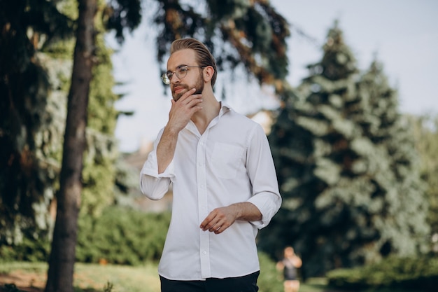 Retrato de jovem barbudo usando óculos e caminhando no parque