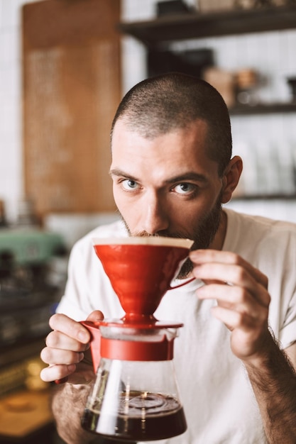 Retrato de jovem barista em pé no balcão do bar e cheirando despeje o café enquanto sonhadoramente olhando para a câmera no café