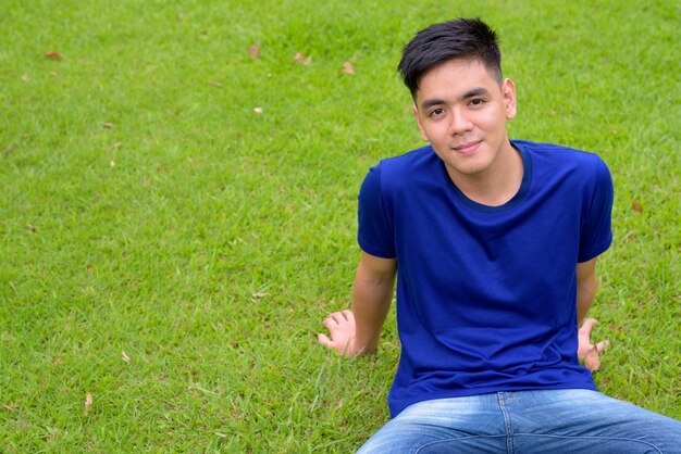 Retrato de jovem bonito asiático relaxando no parque em Bangkok, Tailândia