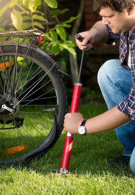 Retrato de jovem bonito bombeando pneus de bicicleta no parque