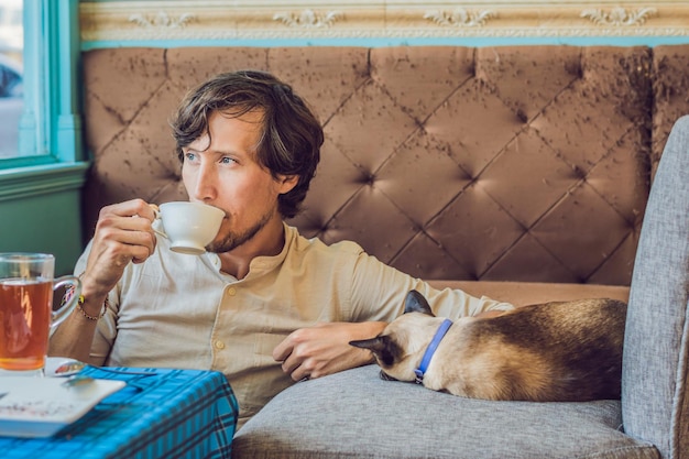 Retrato de jovem bonito, brincando com o gato e bebe café.