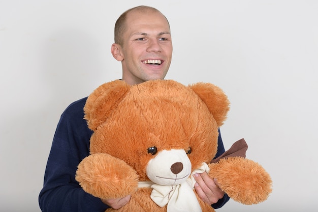 Retrato de jovem bonito careca feliz segurando um grande urso de pelúcia