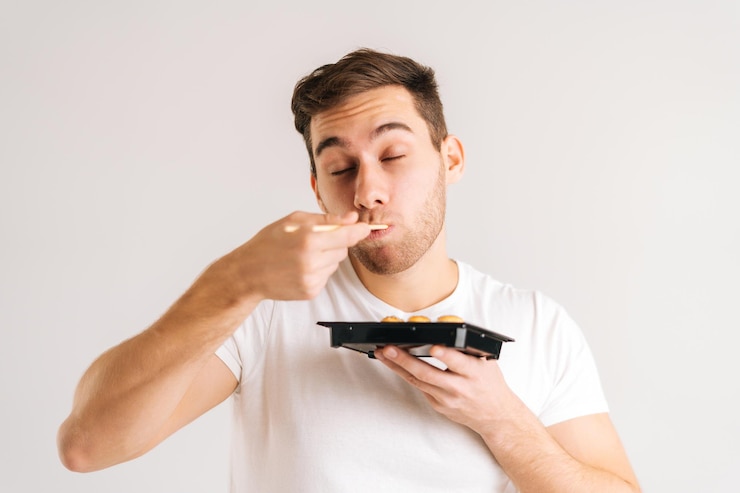 Foto retrato de jovem bonito com os olhos fechados comendo rolos de sushi deliciosos frescos com pauzinhos em fundo branco isolado. foto de estúdio de cara caucasiano feliz come comida tradicional japonesa.