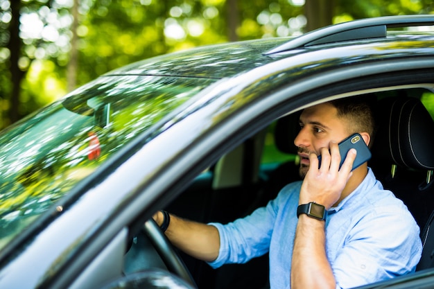 Retrato de jovem bonito dirigindo um carro e falando no celular