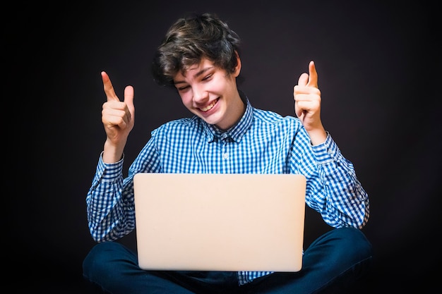 Retrato de jovem bonito e feliz sentado no chão, usar laptop e vestir camisa xadrez e calças b