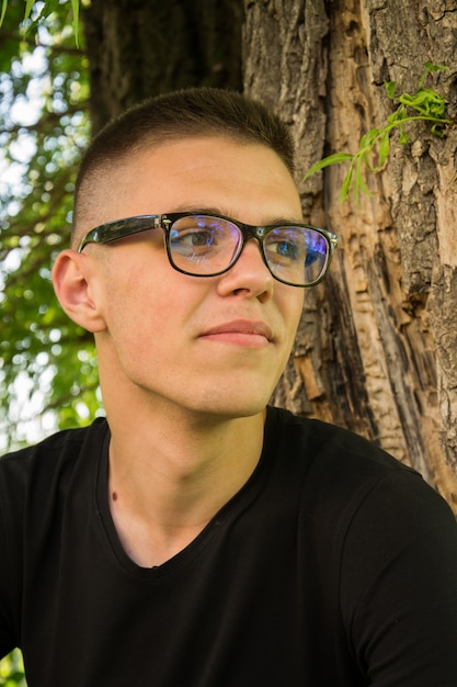 Retrato de jovem bonito e sorridente homem com óculos no parque