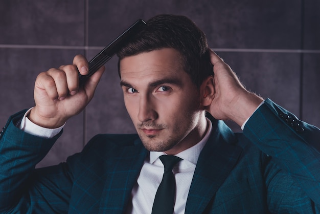 Retrato de jovem bonito em terno preto penteando o cabelo