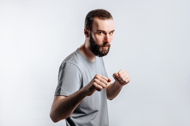 Retrato de jovem bonito franzindo a testa enquanto olha para a câmera com os punhos cerrados e boxe na parede branca