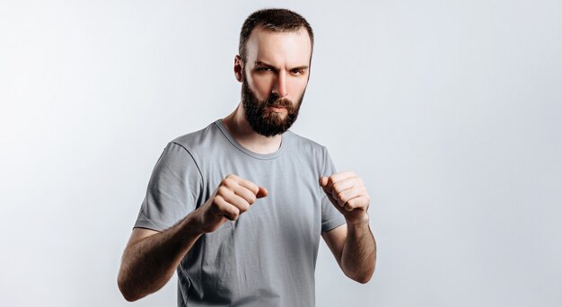 Retrato de jovem bonito franzindo a testa enquanto olha para a câmera com os punhos cerrados e boxe na superfície branca