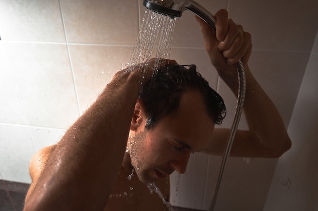 Retrato de jovem bonito se lavando com gel de banho, ensaboando a cabeça com shampoo no banheiro em casa close-up