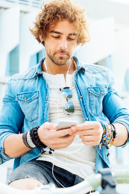 Retrato de jovem bonito, sorrindo quando ele está usando seu celular na rua.