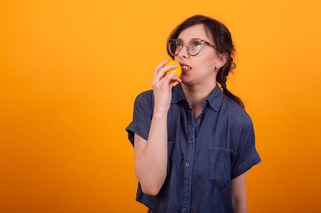 Retrato de jovem bonito surtou com laranja na mão sobre fundo amarelo no estúdio. Menina com deliciosa laranja.