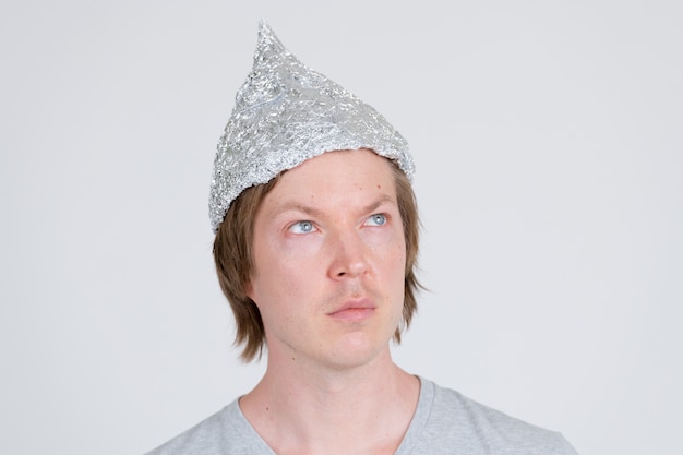 retrato de jovem bonito usando chapéu de papel alumínio como conceito de teoria da conspiração em branco