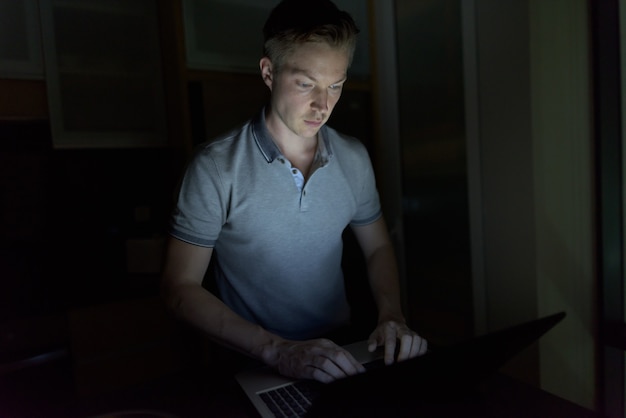 Retrato de jovem bonito usando laptop na sala escura