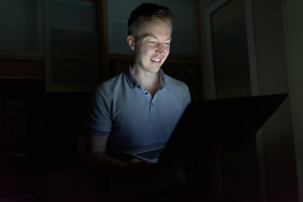 Retrato de jovem bonito usando laptop na sala escura