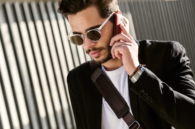 Retrato de jovem bonito usando seu telefone celular na rua.