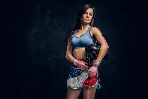 Retrato de jovem boxeador feminino com o capacete nas mãos no estúdio fotográfico escuro.