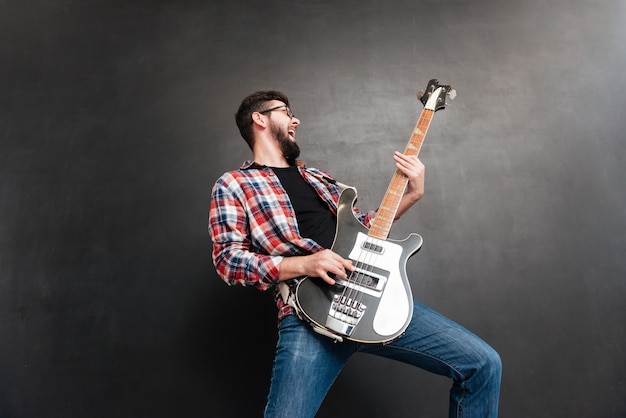 Foto retrato de jovem cantando vestido com uma camisa em uma gaiola de pé na lousa enquanto tocava violão.