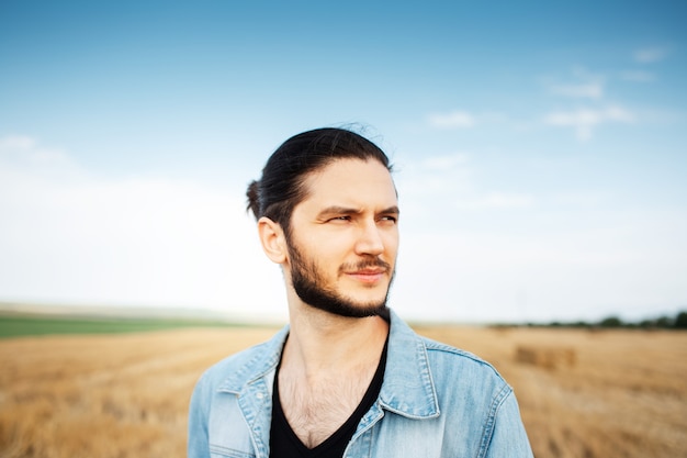 Retrato de jovem cara confiante no fundo do campo de céu e feno turva.