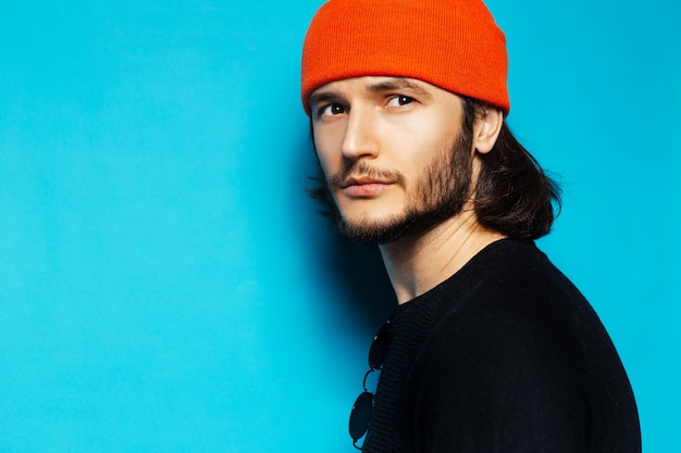 Retrato de jovem cara sério com chapéu laranja sobre fundo azul.