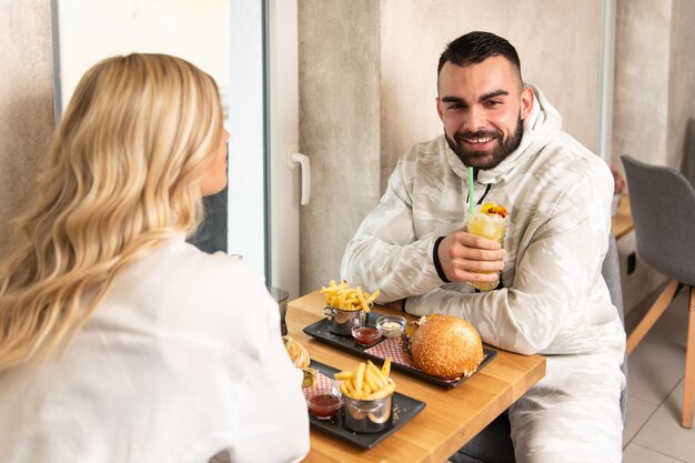 Retrato de jovem casal comendo hambúrguer no restaurante e bebendo coquetel de maracujá mojito