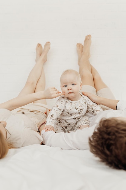 Retrato de jovem casal em roupas brancas, deitado com as pernas levantadas para cima na cama com o bebê