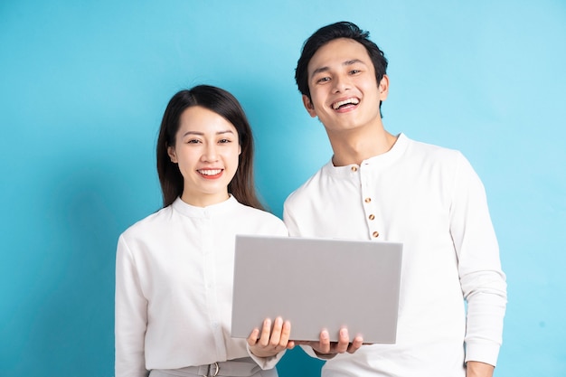 Retrato de jovem casal feliz usando laptop na parede azul