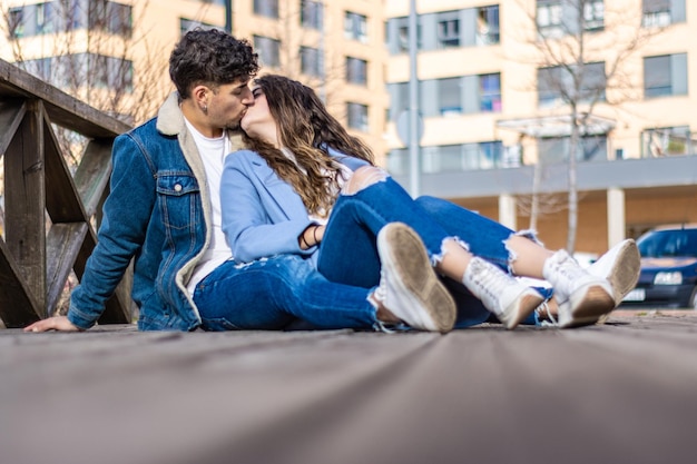 Retrato de jovem casal interracial beijando sentado no chão de madeira ao ar livre