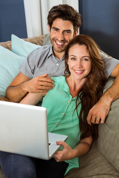 Retrato de jovem casal sentado no sofá e usando o laptop