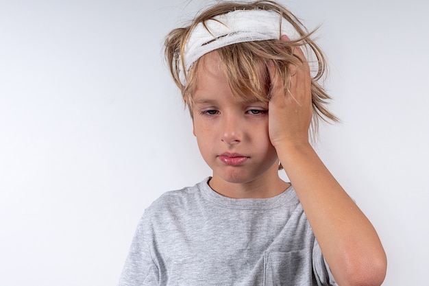 Retrato de jovem caucasiano bonito cabelo loiro com lesão traumática e bandagem na cabeça isolado no fundo branco menino segura sua cabeça com a mão