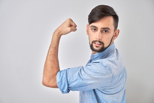 Retrato de jovem caucasiano mostrando bíceps demonstrando poder isolado no fundo branco