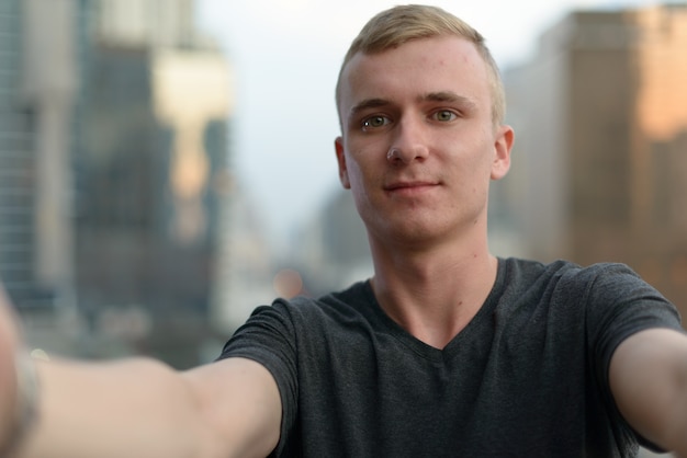 Retrato de jovem com cabelo loiro contra a vista da cidade ao ar livre