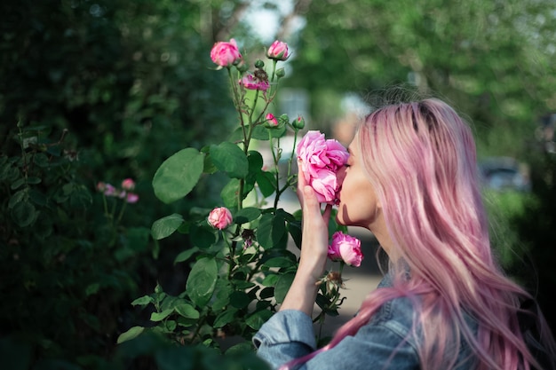 Retrato de jovem com cabelo rosa cheirando flor rosa.