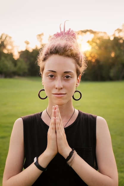 Foto retrato de jovem com dreadlocks rosa fazendo ioga ao ar livre e meditando no parque, pôr do sol. conceito de liberdade e energia