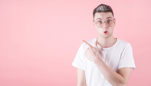 Retrato de jovem com expressão facial chocada apontando para o lado de copyspace com o dedo indicador