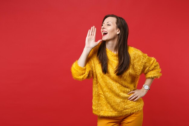 Foto retrato de jovem com suéter de pele amarela olhando de lado falando com um gesto com a mão isolado no fundo da parede vermelha brilhante no estúdio. emoções sinceras de pessoas, conceito de estilo de vida. simule o espaço da cópia.
