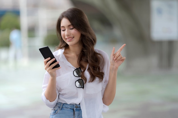 Retrato de jovem com uma carinha sorridente, usando um telefone, caminha por uma cidade