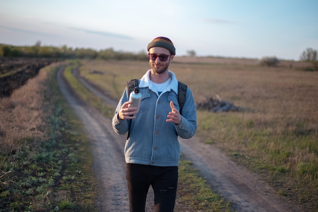 Retrato de jovem com uma mochila segurando uma garrafa térmica de alumínio reutilizável