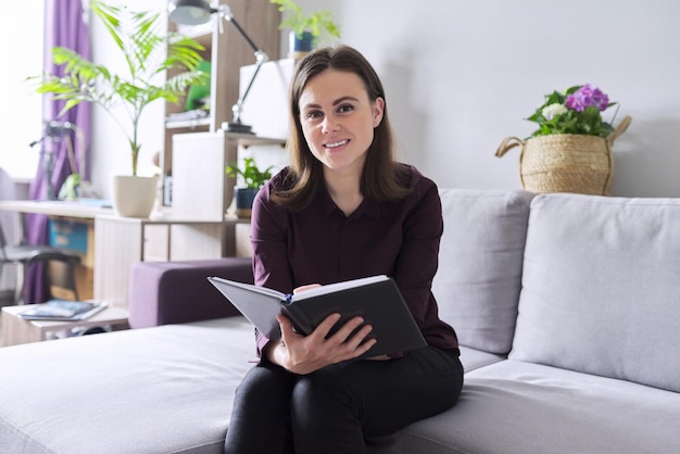 Retrato de jovem consultor feminino sorridente confiante, psicólogo com caderno de negócios, sentado no sofá no escritório. Psicologia, psicoterapia, saúde mental, conceito de ajuda e suporte