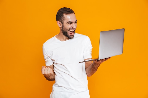 Retrato de jovem de 30 anos em uma camiseta branca segurando um laptop prateado, isolado