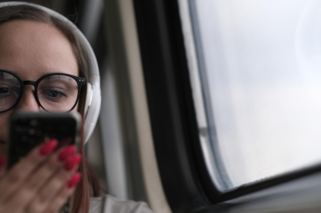 Retrato de jovem de óculos navegando no celular andando de trem close-up pretty feminino usando gadget enquanto está sentado no trem suburbano