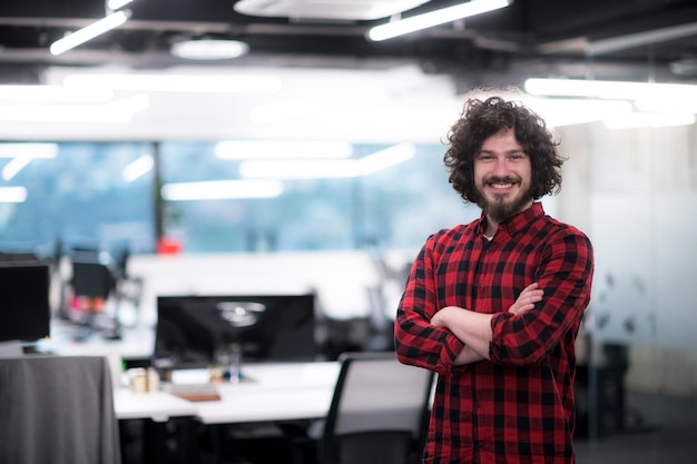 Retrato de jovem desenvolvedor de software masculino bem-sucedido sorridente em pé no escritório de inicialização moderno